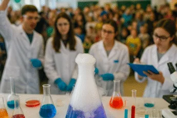 Pokaz eksperymentów chemicznych podczas festiwalu nauki – kolorowe probówki, dymiąca kolba i młodzi naukowcy w białych fartuchach