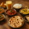 Zestaw kolorowych indyjskich dań na drewnianym stole – naan, curry, ryż i mango lassi w stylu tilt-shift, sfotografowane w poziomie.