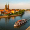 Statek pasażerski z turystami płynący Odrą we Wrocławiu na tle Ostrowa Tumskiego i mostów w centrum miasta
