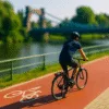 Rowerzysta jadący czerwoną ścieżką rowerową wzdłuż Odry we Wrocławiu, z mostem w tle