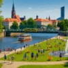 Rodziny z dziećmi bawiące się w fontannie i na trawie nad Odrą we Wrocławiu w letnie popołudnie, w tle tramwaj i statek pasażerski