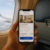 Smartfon z otwartą aplikacją rezerwacji hotelu trzymany w dłoni pasażera w samolocie – eSIM i mobilne podróżowanie za granicą