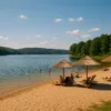 Letni krajobraz nad jeziorem w Czechach – plaża, woda, parasole i zielone wzgórza w tle