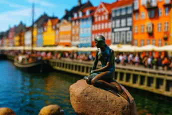 The Statue of the Little Mermaid against the background of colorful nyhavn tenement houses in the Tilt-Shift style, rapprochement from the perspective of the quay