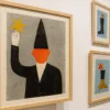Wystawa grafik w Centrum Kultury Nowy Pafawag – plakat z sylwetką w czarnym stroju i pomarańczową twarzą na tle szarym, obok inne ilustracje w ramkach