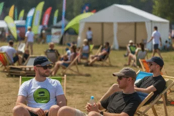 Uczestnicy festiwalu na leżakach podczas letniego wydarzenia plenerowego we Wrocławiu, z kolorowymi flagami i namiotami w tle