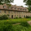 Dwupiętrowy budynek mieszkalny z lat 40. XX wieku otoczony bujną zielenią i kwitnącymi liliowcami w stylu przedmieścia-ogrodu