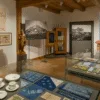 Widok wystawy w muzeum etnograficznym, z porcelaną, materiałami blaudruk, mapą Śląskiej Kolei Górskiej i drewnianą rzeźbą w sali oświetlonej światłem dziennym