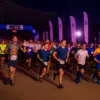 Start nocnego półmaratonu na Stadionie Olimpijskim we Wrocławiu – szeroki kadr z perspektywy prawej strony, z tłumem biegaczy ruszających spod łuku META, w świetle wieczornych reflektorów i flag wydarzenia