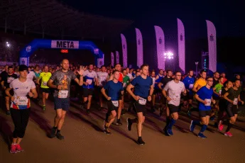 Start nocnego półmaratonu na Stadionie Olimpijskim we Wrocławiu – szeroki kadr z perspektywy prawej strony, z tłumem biegaczy ruszających spod łuku META, w świetle wieczornych reflektorów i flag wydarzenia