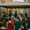 Koncert na świeżym powietrzu na wrocławskiej ulicy – zespół występuje pod namiotem dla zgromadzonej publiczności, w tle kolorowe kamienice