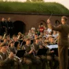 Koncert wojskowej orkiestry na Bastionie Sakwowym we Wrocławiu, publiczność siedzi na trawie podczas zachodu słońca